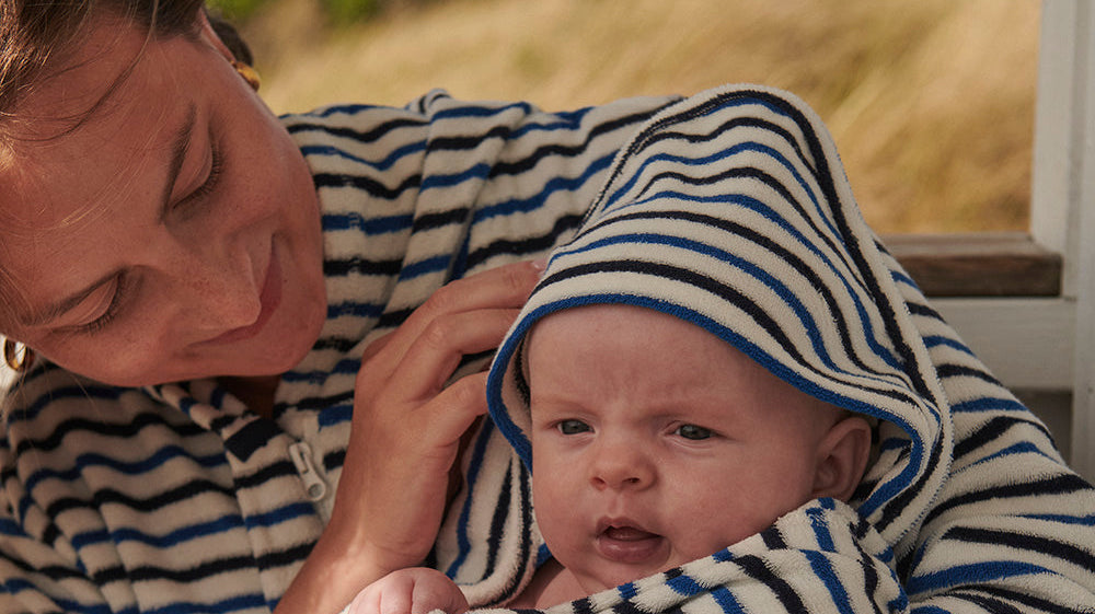 Nyfödd baby insvept i randig handduk med huva i en förälders famn